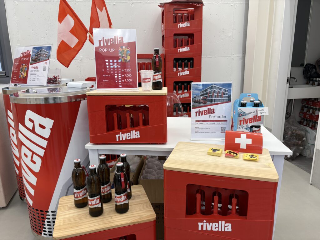 HELLO SeongSuマーケット4階 Rivella（リヴェラ）ポップアップブース スイス国旗と赤いロゴクレートが並ぶ試飲・販売コーナー