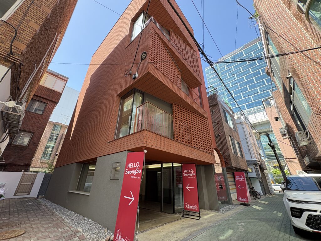 HELLO SeongSuマーケット会場・イサクビル全景 赤い幟と誘導サインが並ぶ聖水の路地 4階建て赤レンガ外観