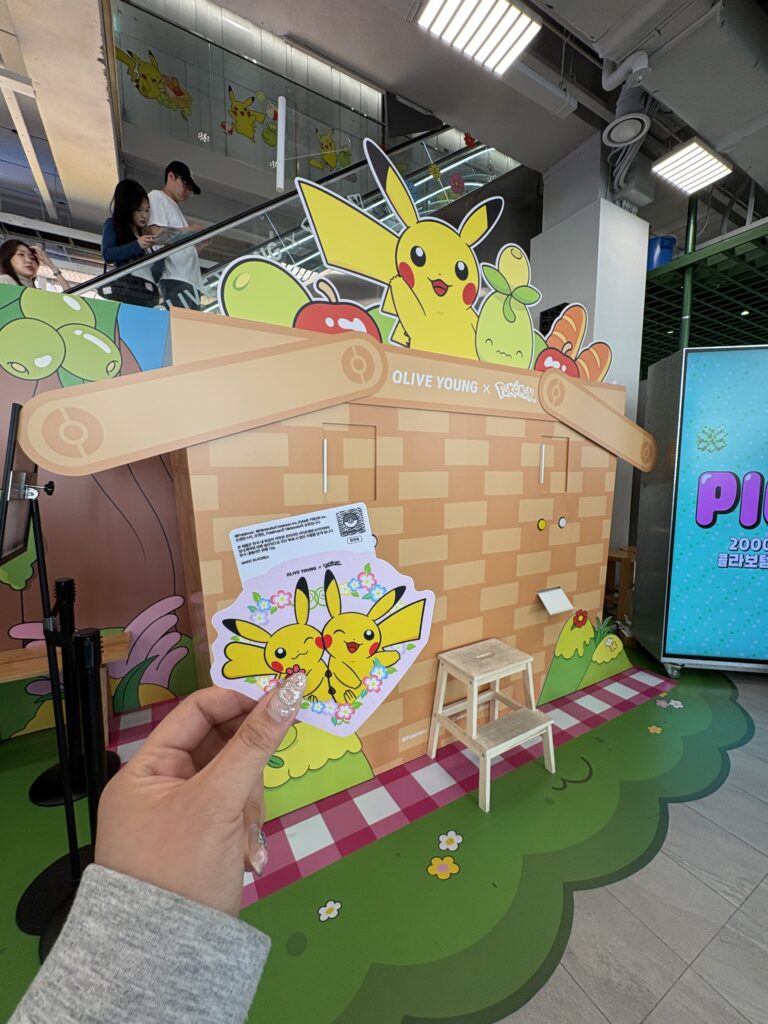 OLIVE YOUNG×ポケモンコラボ聖水 ピカチュウフォトゾーンとピクニックテーマのフォトスポット 来場記念カードを手に持つ様子